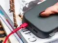 Dłoń z czerwonymi paznokciami podtrzymuje power bank 50000 mah na ile starcza, podłączony czerwonym kablem.