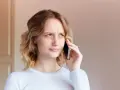Zmarszczona kobieta rozmawia przez telefon, próbując dowiedzieć się, jak zwiększyć głośność w telefonie, bo rozmówca mówi za cicho.