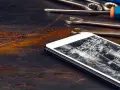 Zepsuty ekran telefonu leży obok narzędzi. Pęknięcia tworzą pajęczynę na szkle.