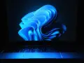 Niebieski, falujący kształt na ekranie laptopa z podświetlaną klawiaturą, przypominający logo Windows 11 24H2.