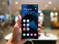 Dłoń trzyma smartfon z interfejsem One UI 6, prezentującym ekran startowy Galaxy S24 Ultra z ikonami aplikacji.
