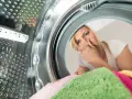 Kobieta zatyka nos, czując brzydki zapach z pralki. W środku widać kolorowe ręczniki.