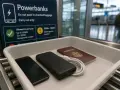 Na lotnisku, na taśmie do kontroli bezpieczeństwa, leżą telefon, powerbank i paszport. Znak informuje, jaki powerbank do samolotu można zabrać.