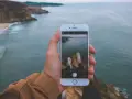 Dłoń trzyma iPhone'a 15, na ekranie widok klifów i oceanu. Czy iPhone 15 jest wodoszczelny? To pytanie zadaje sobie wielu podróżników.
