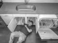 Mężczyzna pod zlewem sprawdza, jak sprawdzić elektrozawór w zmywarce, która jest otwarta.