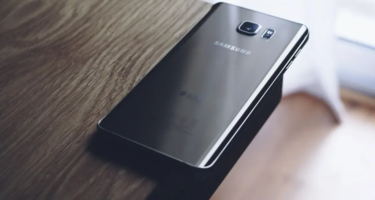 Czarny Samsung leży na drewnianym blacie. Chcesz wiedzieć, jak zresetować telefon Samsung?
