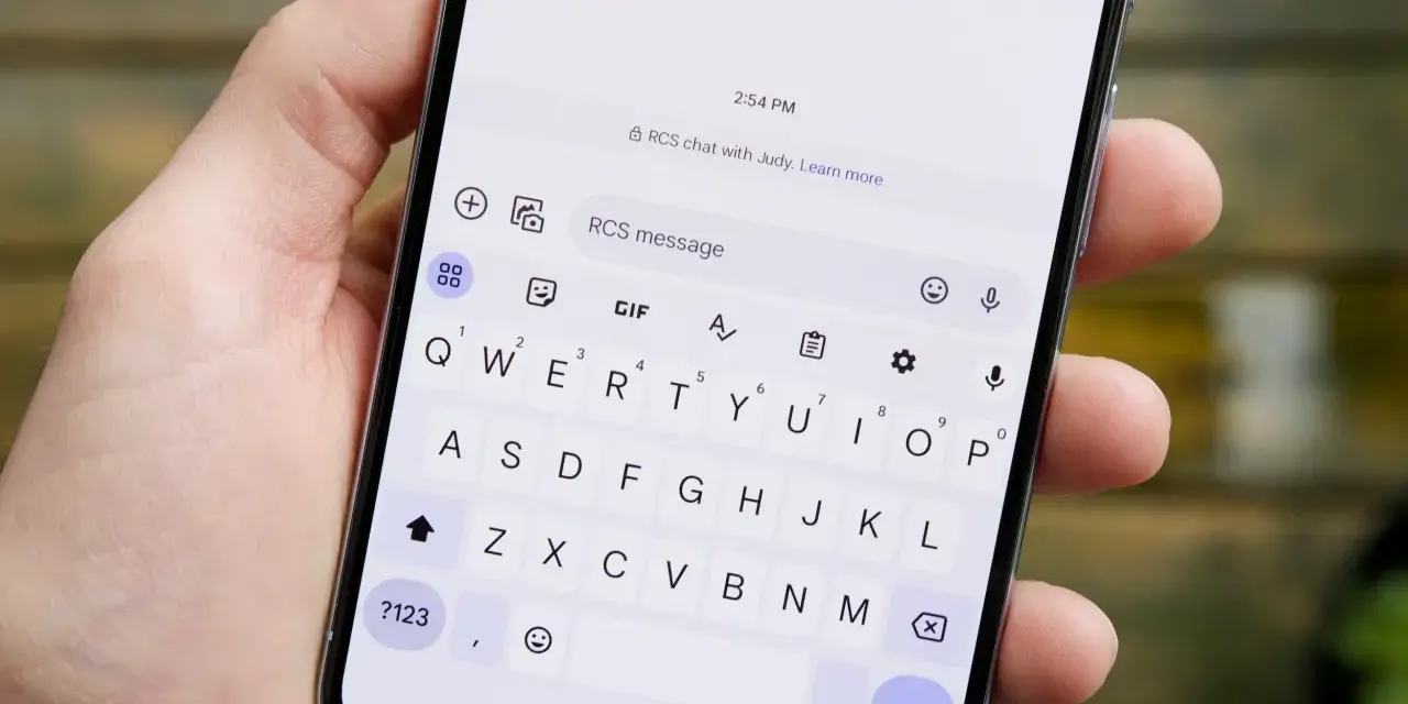 Dłoń trzyma smartfon z otwartą klawiaturą. Widoczny komunikat "RCS chat with Judy" sugeruje, jak włączyć czat RCS.