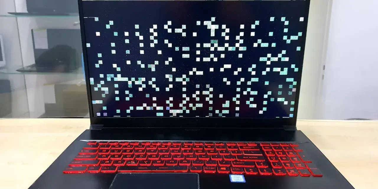 Laptop z artefaktami na ekranie, wskazującymi na problemy z kartą graficzną. Klawiatura podświetlona na czerwono.