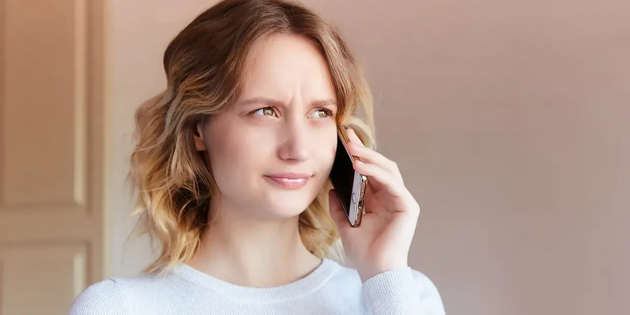 Zmarszczona kobieta rozmawia przez telefon, próbując dowiedzieć się, jak zwiększyć głośność w telefonie, bo rozmówca mówi za cicho.