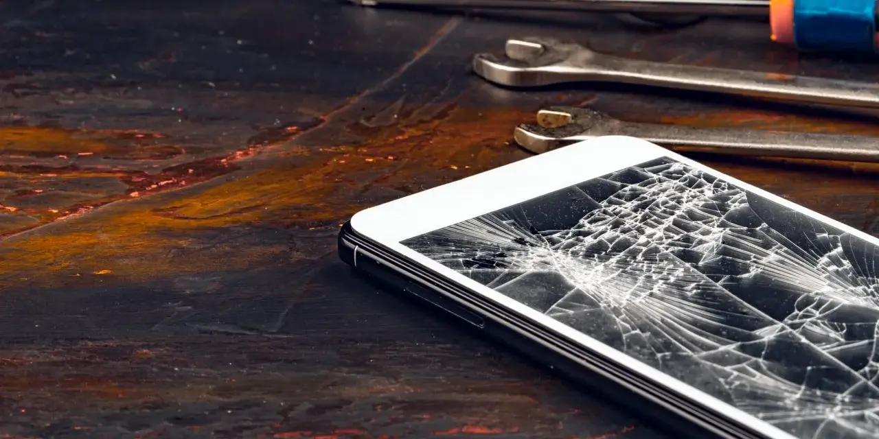 Zepsuty ekran telefonu leży obok narzędzi. Pęknięcia tworzą pajęczynę na szkle.
