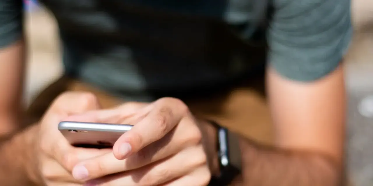 Mężczyzna trzyma smartfon, a na jego nadgarstku widać smartwatch. Właśnie sprawdza, jak sparować zegarek z telefonem.