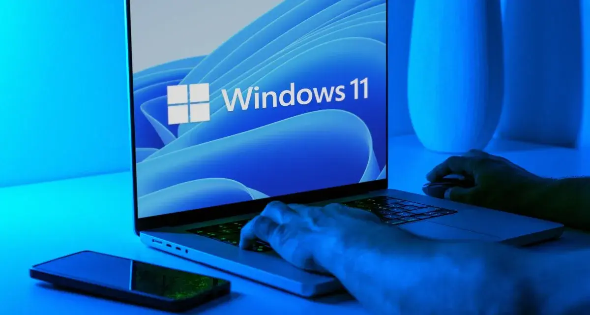 Ręce na klawiaturze laptopa z logo Windows 11. Dowiedz się, jak wejść do BIOS-u Windows 11, aby dostosować ustawienia.