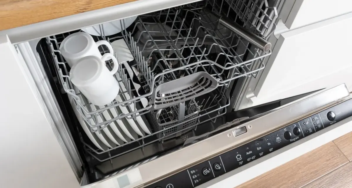 Wnętrze zmywarki Whirlpool 6th Sense z koszami pełnymi naczyń, w tym kubków i talerzy.
