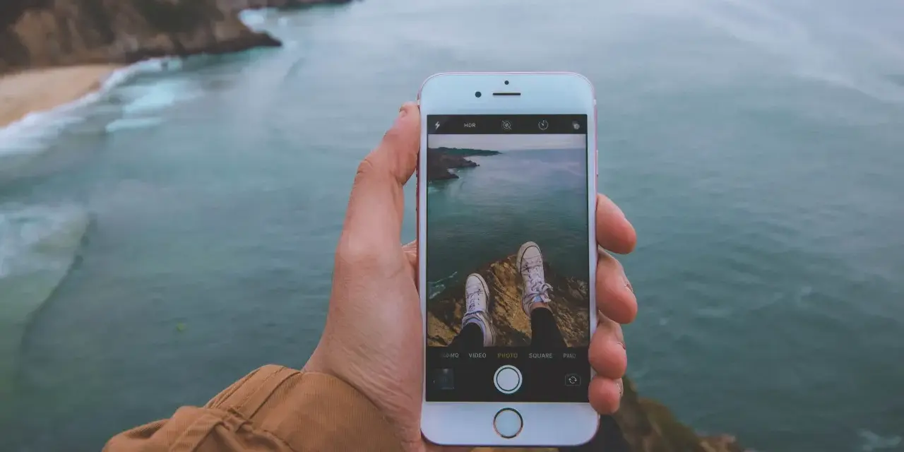 Dłoń trzyma iPhone'a 15, na ekranie widok klifów i oceanu. Czy iPhone 15 jest wodoszczelny? To pytanie zadaje sobie wielu podróżników.