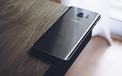 Czarny Samsung leży na drewnianym blacie. Chcesz wiedzieć, jak zresetować telefon Samsung?
