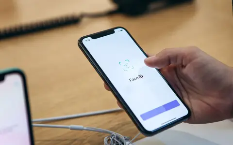 Dłoń trzyma smartfon, na ekranie którego wyświetla się komunikat "Face ID". Wygląda na to, że Face ID nie działa.