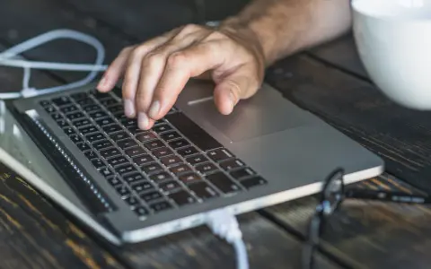 Dłoń na klawiaturze laptopa, przygotowująca się do twardego resetu. Obok biały kubek.