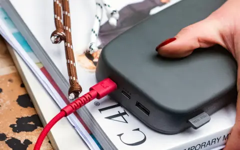Dłoń z czerwonymi paznokciami podtrzymuje power bank 50000 mah na ile starcza, podłączony czerwonym kablem.