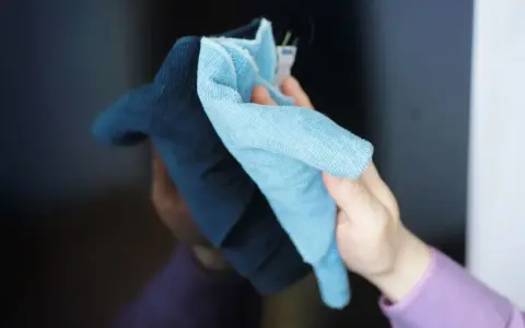 Delikatne mikrofibry to klucz do pytania: czym umyć ekran telewizora. Ręka z dwoma ściereczkami czyści czarny ekran.