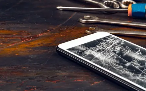Zepsuty ekran telefonu leży obok narzędzi. Pęknięcia tworzą pajęczynę na szkle.