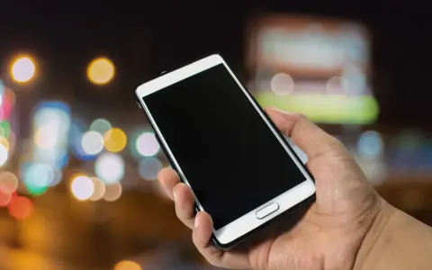 Dłoń trzyma smartfon Samsung. Zastanawiasz się, jak wyłączyć telefon Samsung bez dotyku? Oto rozwiązanie.