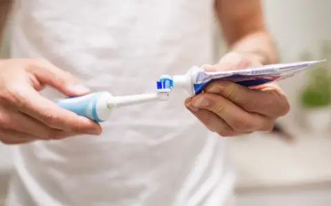 Przygotowanie do mycia zębów szczoteczką soniczną: nakładanie pasty na główkę.