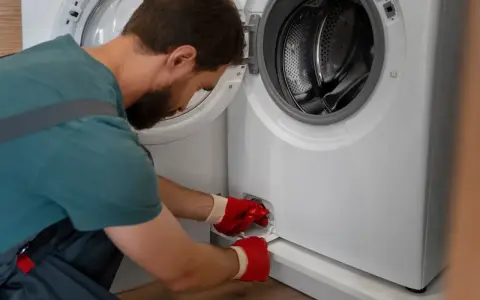 Mężczyzna w czerwonych rękawiczkach otwiera klapkę pralki, przygotowując się do jej czyszczenia. To pierwszy krok, jak odkamienić pralkę.