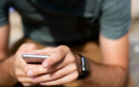 Mężczyzna trzyma smartfon, a na jego nadgarstku widać smartwatch. Właśnie sprawdza, jak sparować zegarek z telefonem.
