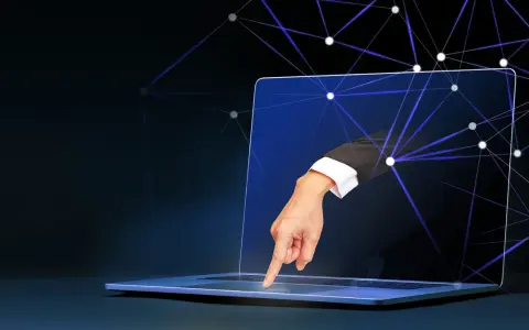 Ręka w garniturze wychodzi z ekranu laptopa, dotykając klawiatury. Sieć połączeń symbolizuje zdalny dostęp do komputera.