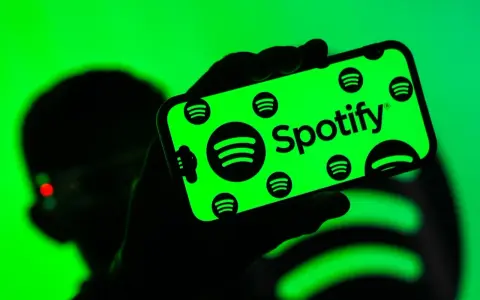 Dłoń trzyma smartfon z zielonym ekranem, na którym widnieje logo Spotify. Użytkownik cieszy się doskonałą spotify jakość dźwięku.