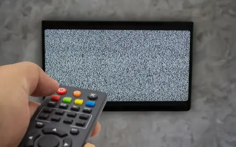Ręka trzyma pilot dekodera, celując w ekran telewizora z zakłóceniami. Czas na naukę, jak sparować pilot dekodera z telewizorem.