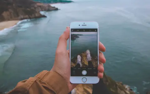 Dłoń trzyma iPhone'a 15, na ekranie widok klifów i oceanu. Czy iPhone 15 jest wodoszczelny? To pytanie zadaje sobie wielu podróżników.