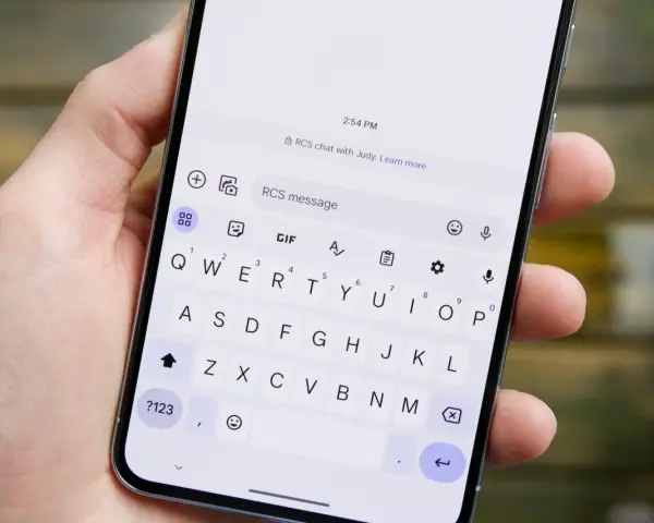 Dłoń trzyma smartfon z otwartą klawiaturą. Widoczny komunikat "RCS chat with Judy" sugeruje, jak włączyć czat RCS.