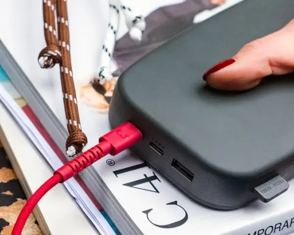 Dłoń z czerwonymi paznokciami podtrzymuje power bank 50000 mah na ile starcza, podłączony czerwonym kablem.
