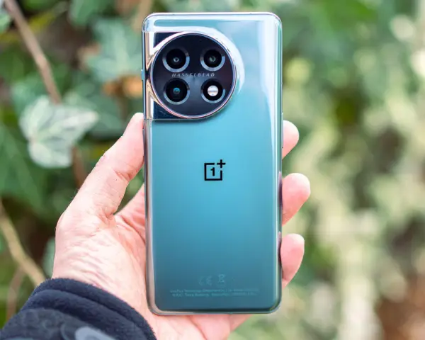 Dłoń trzyma zielony telefon z okrągłym aparatem Hasselblad.
