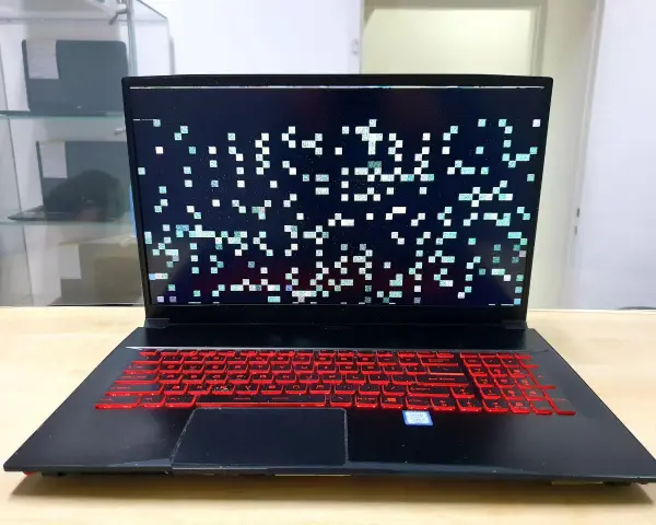 Laptop z artefaktami na ekranie, wskazującymi na problemy z kartą graficzną. Klawiatura podświetlona na czerwono.