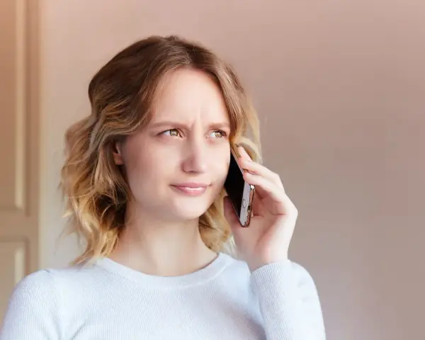 Zmarszczona kobieta rozmawia przez telefon, próbując dowiedzieć się, jak zwiększyć głośność w telefonie, bo rozmówca mówi za cicho.