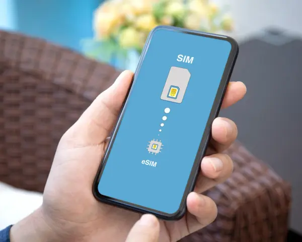 Dłoń trzyma smartfon z wyświetloną grafiką porównującą tradycyjną kartę SIM z technologią eSIM.