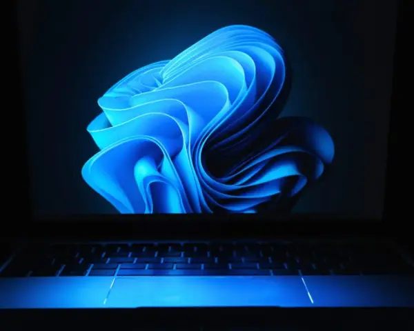 Niebieski, falujący kształt na ekranie laptopa z podświetlaną klawiaturą, przypominający logo Windows 11 24H2.