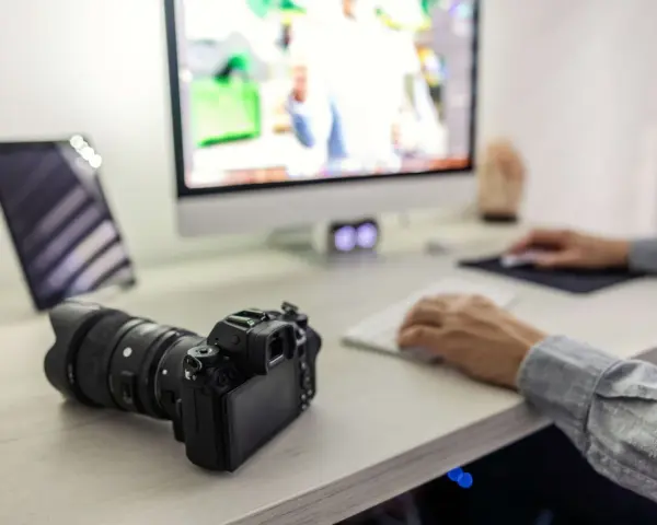 Aparat fotograficzny i tablet na biurku, obok komputera. Ułatwia to proces, jak przegrać zdjęcia z telefonu na komputer.