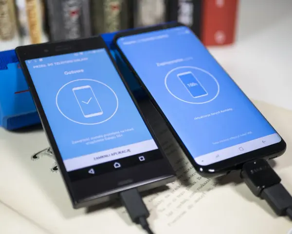 Dwa telefony połączone kablem USB. Jeden pokazuje "Gotowe", drugi "100%". To pokazuje, jak przenieść dane z telefonu na telefon.