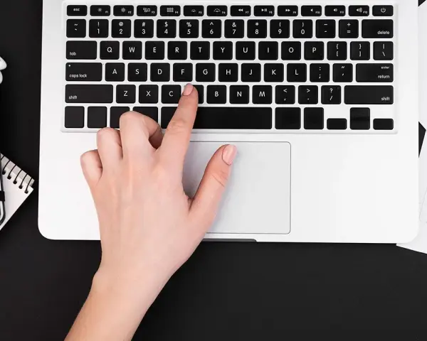 Dłoń naciska klawisz "C" na klawiaturze laptopa, co może być przyczyną, dlaczego nie działa klawiatura w laptopie.