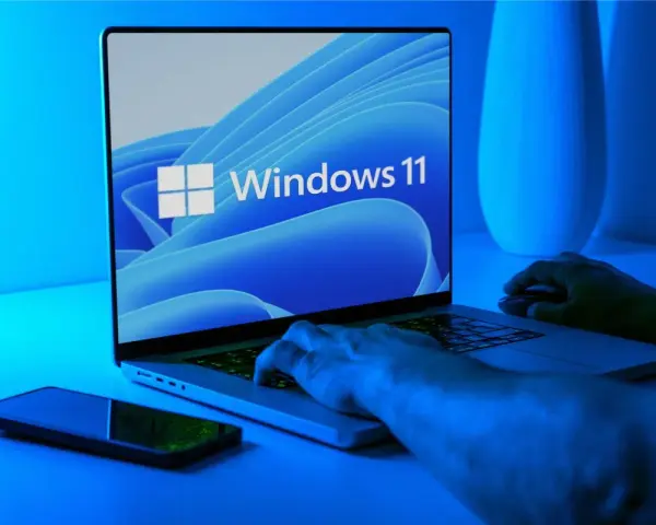 Ręce na klawiaturze laptopa z logo Windows 11. Dowiedz się, jak wejść do BIOS-u Windows 11, aby dostosować ustawienia.
