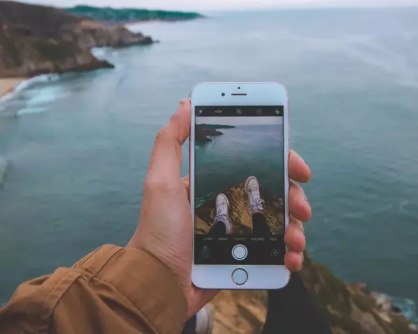 Dłoń trzyma iPhone'a 15, na ekranie widok klifów i oceanu. Czy iPhone 15 jest wodoszczelny? To pytanie zadaje sobie wielu podróżników.