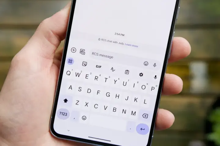 Dłoń trzyma smartfon z otwartą klawiaturą. Widoczny komunikat "RCS chat with Judy" sugeruje, jak włączyć czat RCS.
