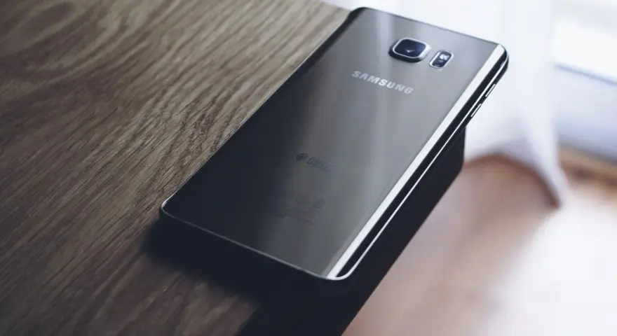 Czarny Samsung leży na drewnianym blacie. Chcesz wiedzieć, jak zresetować telefon Samsung?