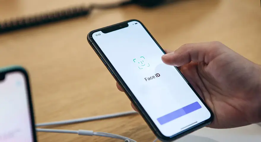 Dłoń trzyma smartfon, na ekranie którego wyświetla się komunikat "Face ID". Wygląda na to, że Face ID nie działa.