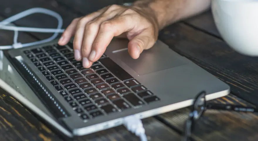 Dłoń na klawiaturze laptopa, przygotowująca się do twardego resetu. Obok biały kubek.