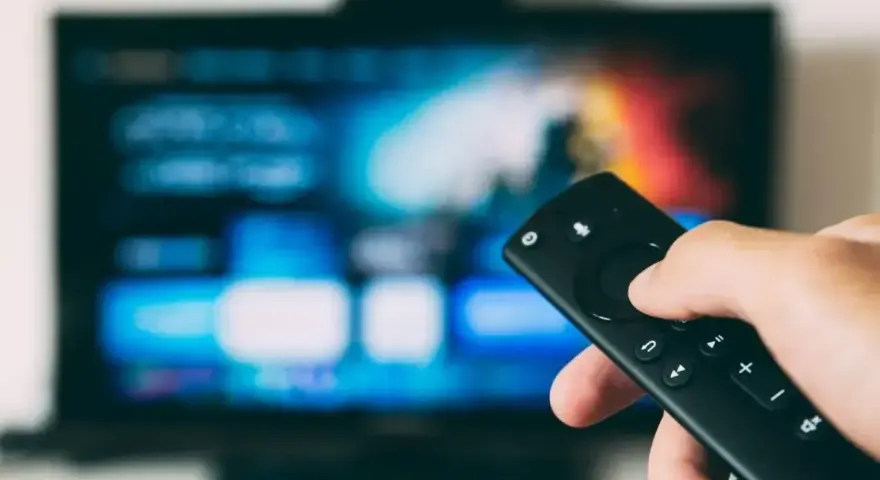 Dłoń trzymająca pilot do telewizora LG, ekran pokazuje menu. Dowiedz się, jak wyłączyć lektora w telewizorze LG.
