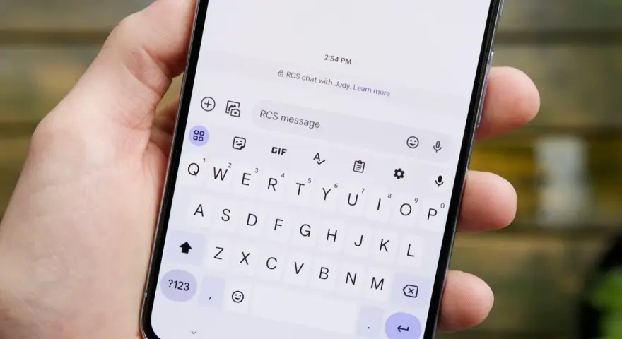Dłoń trzyma smartfon z otwartą klawiaturą. Widoczny komunikat "RCS chat with Judy" sugeruje, jak włączyć czat RCS.